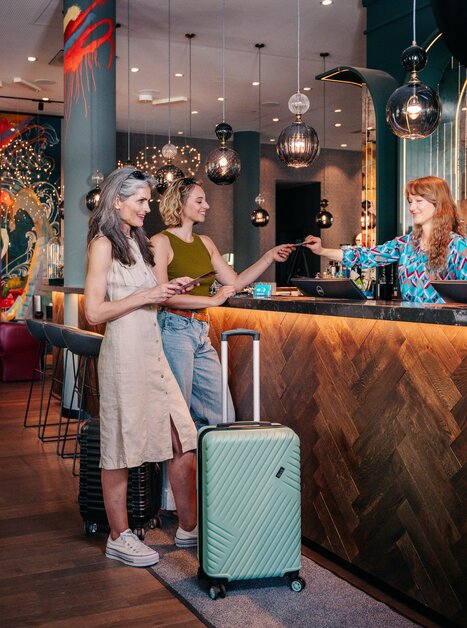 Two women are at the reception with their luggage as an employee processes the check-in. | © Graz Tourismus - Mias Photoart